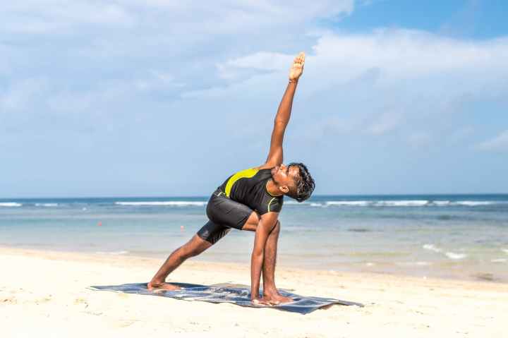 man doing yoga pose on blue mat beside seashore